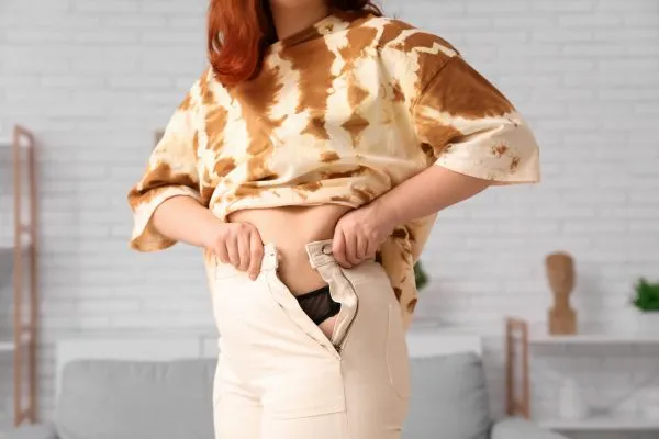 Image of woman trying to do her trousers up after pregnancy weight gain Greenock