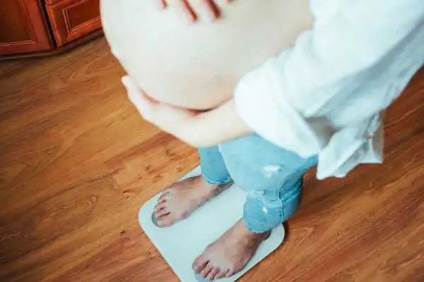 Image of woman weighing herself and experiencing weight gain through pregnancy Greenock